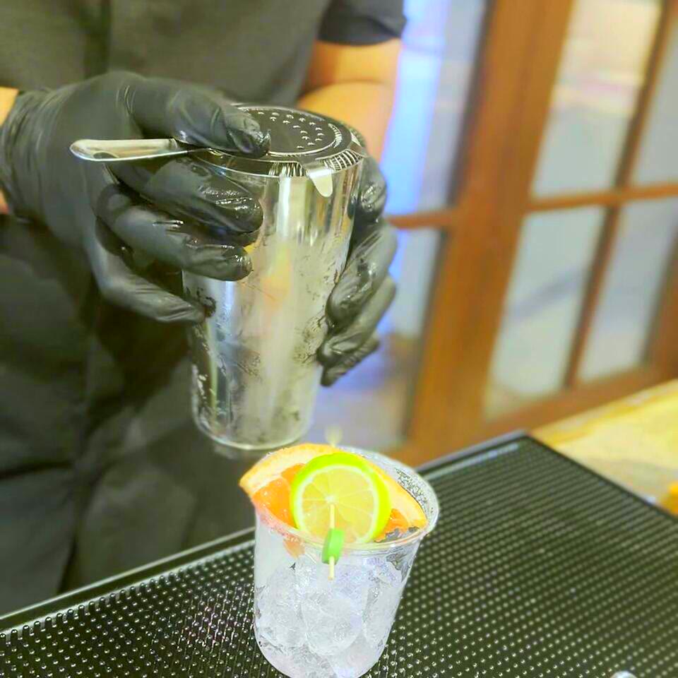 A bartender straining a fresh-shaken drink into an ice-filled cup garnished with grapefruit and lime