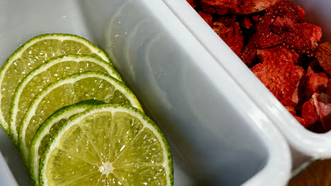 The garnish station in close-up: fresh-cut lime wheels and dried strawberries in white caddies