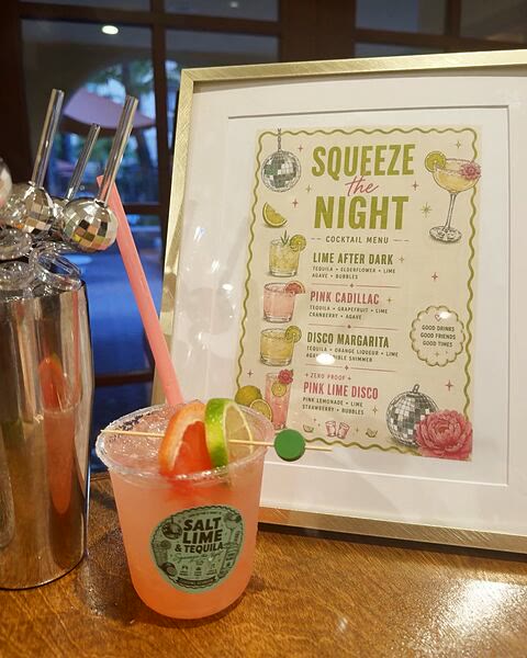 The client&rsquo;s printed cocktail menu, framed and standing on the bar, a finished pink cocktail in a stickered cup in front of it