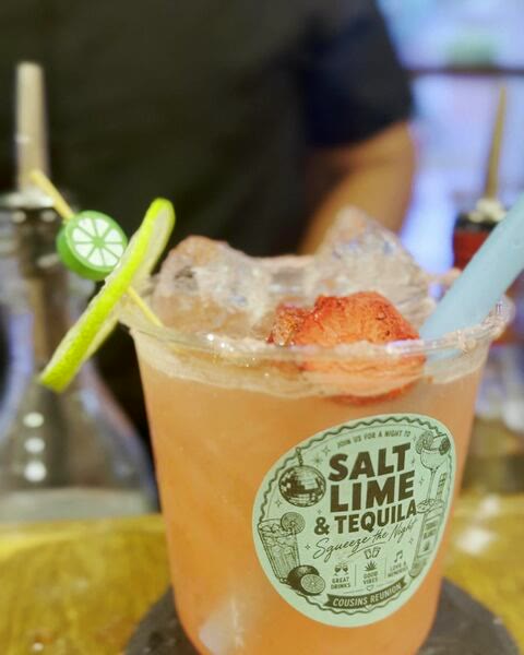 Finished cocktail with a salted rim and lime and strawberry garnish, in a cup carrying the event's custom sticker