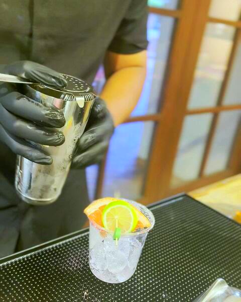 Salt Rim bartender in black with service gloves straining a cocktail from a shaker into a garnished cup